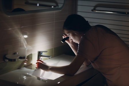Woman young holding hand flashlight in darkness at kitchen sink and faucetの写真素材