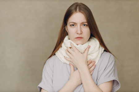 Young woman holding throat wearing scarf flu catarrh ill sick disease treatment coldの写真素材