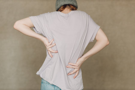 Young woman with back spine pain ache against brown backgroundの写真素材
