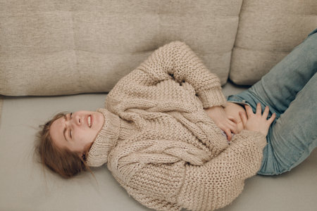 Young woman with stomach abdominal pain ache lying on sofaの写真素材