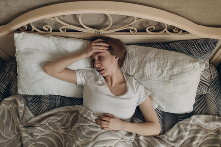 Young woman with headache flu ill sick disease cold at home indoor lying on bedの写真素材