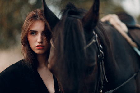 Young woman in black with her horse at sunset outdoorsの写真素材