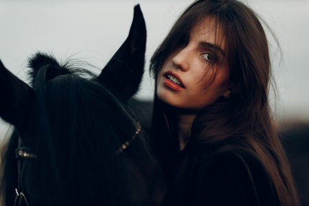 Young woman in black with her horse at sunset outdoorsの写真素材