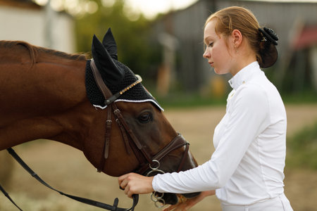 Jockey female rider portrait in white uniform holds bridle of dressage horse at stableの写真素材