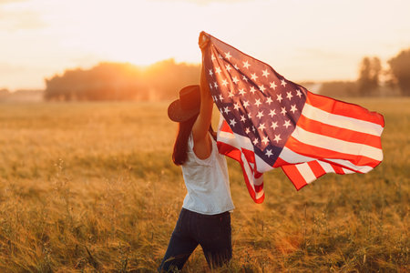 Patriotic Independence day 4th of July Woman farmer in the agricultural field with american flag on sunset.の写真素材