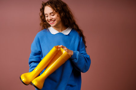 Young positive smiling girl holds in her hands a waterproof rubber boots. Autumn concept.の写真素材