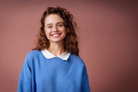 Happy smiling young adult woman wearing autumn blue sweater casual outfit indoors looking at cameraの写真素材