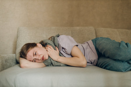 Young woman wearing scarf has flu ill sick disease cold at home indoor lying on sofaの写真素材