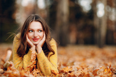 Young woman lies in autumn park ground with yellow foliage maple leaves aroundの写真素材