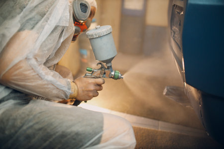 Car painter in protective clothes and respirator mask painting vehicle