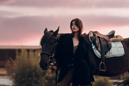 Young woman in black with her horse at sunset outdoorsの写真素材