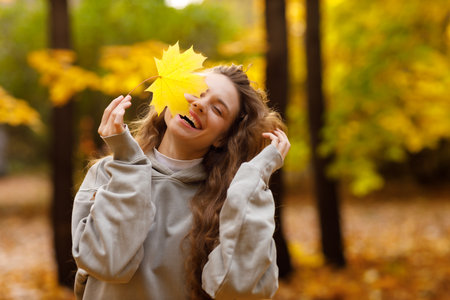 Young laughing woman holds yellow leaf in her hand in the park at sunsetの写真素材