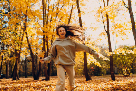 Smiling young woman plays and jumping dancing in the autumn forest with the yellow leaves at sunsetの写真素材
