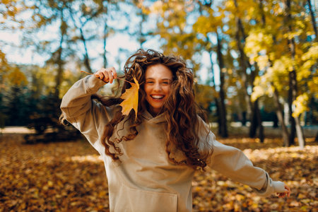 Smiling young woman enjoys the autumn weather in the forest with the yellow leaves at sunset