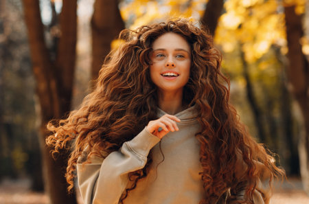 Smiling young woman enjoying the autumn season in the fall park with the yellow leaves at sunsetの写真素材