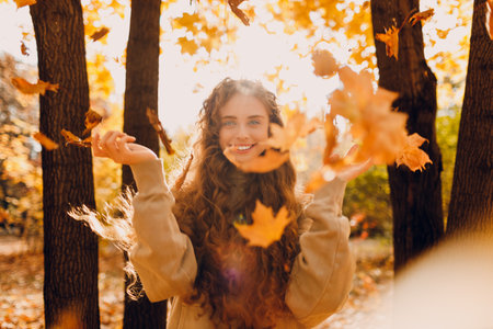 Smiling young woman throws up the yellow autumn leaves in the forest at sunsetの写真素材