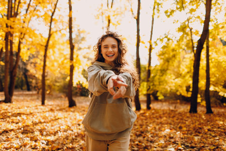 Smiling young woman enjoys the autumn weather in the forest with the yellow leaves at sunsetの写真素材