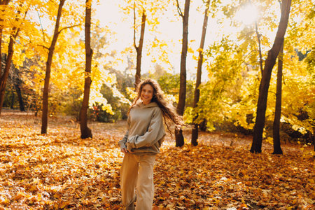 Smiling young woman plays and jumping dancing in the autumn forest with the yellow leaves at sunset