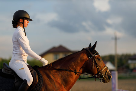 Woman rider jockey profile in helmet and white uniform preparing horse racingの写真素材