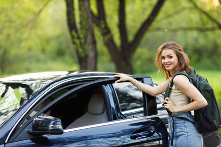 Happy woman driver at car with backpack. Cute young happy brunette female driving car vehicle in summerの写真素材