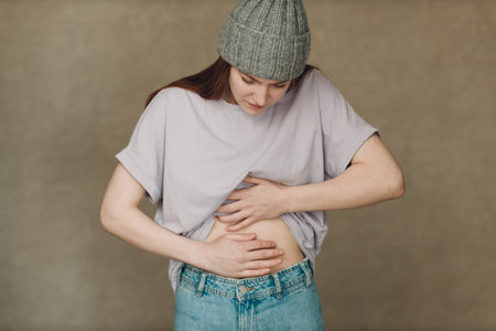Young woman with stomach pain ache against brown backgroundの写真素材