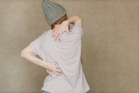 Young woman with back spine pain ache against brown backgroundの写真素材
