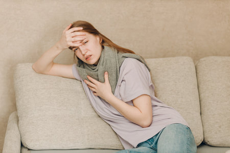 Young woman wearing scarf has flu ill sick disease cold at home indoor on sofaの写真素材