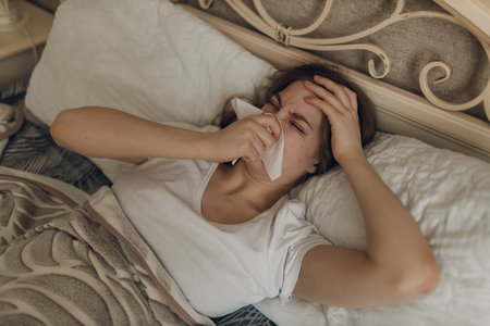 Young woman wearing scarf has flu ill sick disease common cold at home indoor lying on bedの写真素材