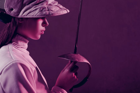 Young woman fencer profile portrait with fencing equipment holding sword in handの写真素材
