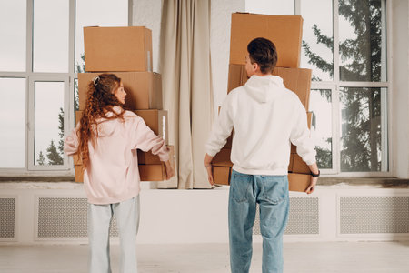 Happy young family couple man and woman moving with cardboard boxes to new estate home apartment. Rear back view.の写真素材