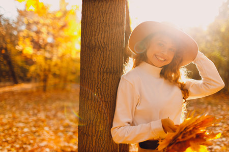 Smiling young woman in the hat enjoys the autumn weather in the forest with the yellow leaves at sunset treeの写真素材