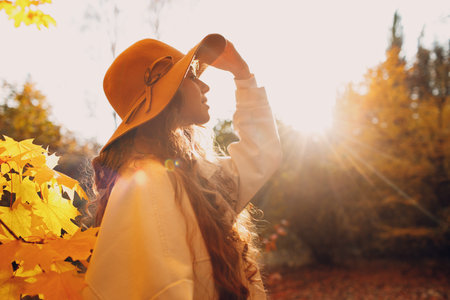Smiling young woman profile portrait in the autumn forest with the yellow leaves at sunsetの写真素材