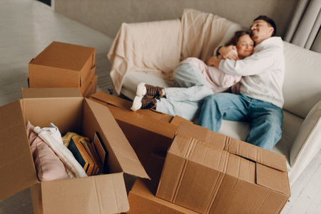 Happy young family couple man and woman relaxing on sofa after moving cardboard boxes to new estate home apartment. Selective focus.の写真素材