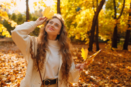 Smiling young woman holds yellow leaf in her hand in the park at sunset with copy spaceの写真素材