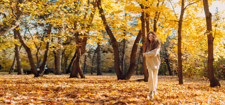 Smiling running woman plays and jumping dancing in the autumn forest with the yellow leaves at sunset. Copy space.の写真素材