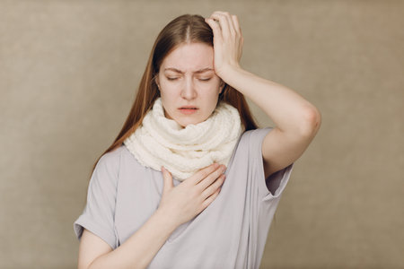 Young woman wearing scarf holds head flu catarrh ill sick disease treatment coldの写真素材
