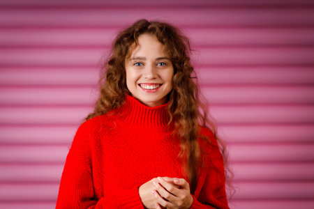 Happy smiling young adult woman wearing winter warm red sweater indoors looking at camera with joyful smileの写真素材