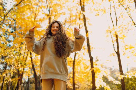 Smiling young woman plays and jumping dancing in the autumn park with the yellow leaves at sunsetの写真素材
