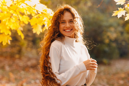Smiling young woman enjoy the autumn weather in the parkland with the yellow leaves at branchesの写真素材