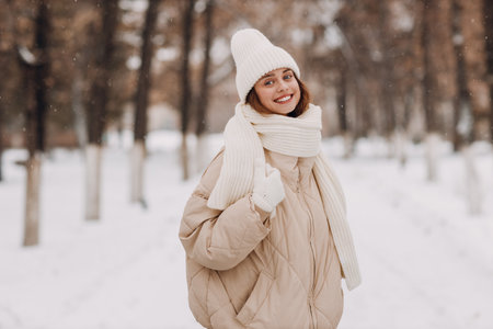 Happy smiling young woman portrait dressed coat scarf hat and mittens enjoys winter weather walking at snowy winter parkの写真素材