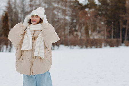 Happy smiling young woman portrait dressed coat scarf hat and mittens enjoys winter weather at snowy winter forestの写真素材