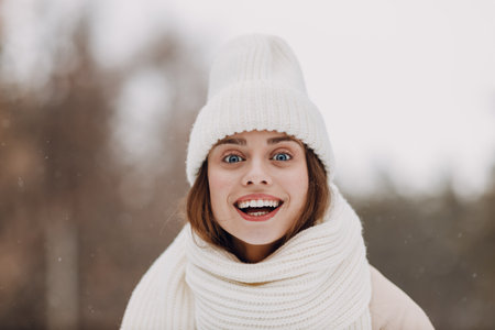 Happy smiling young woman close up portrait dressed coat scarf hat and mittens enjoys winter weather at snowy winter parkの写真素材
