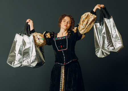 Portrait of a young adult woman dressed in a medieval dress holding shopping bags in handsの写真素材