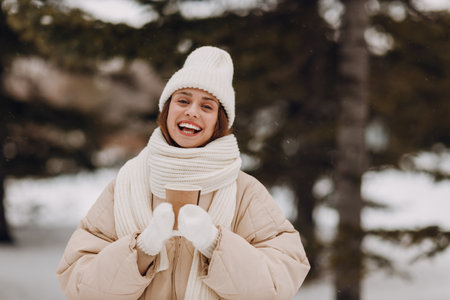 Smiling young woman with coffee hot drink cup enjoys winter weather at snowy winter parkの写真素材
