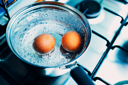 Saucepan stainless steel with two boiling eggs breakfast in a water on a gas stove top view.の写真素材