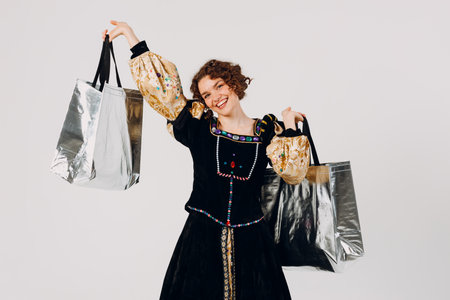 Young adult woman dressed in a medieval dress holding shopping bags in hands isolated white backgroundの写真素材