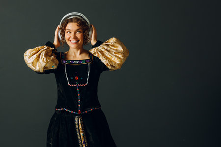 Portrait of a young aristocratic woman with headphones and touching head and dressed in a medieval dress listens musicの写真素材