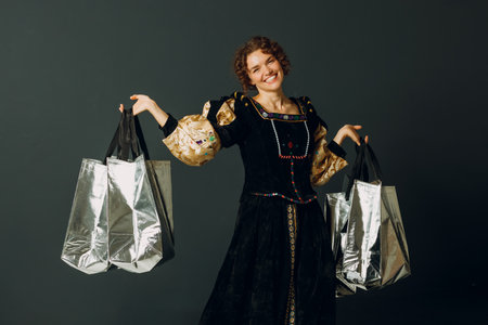 Portrait of a smiling young adult woman dressed in a medieval dress holding shopping bags in handsの写真素材