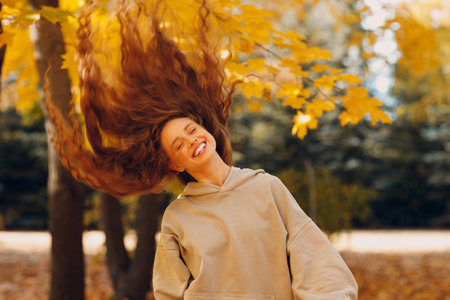 Smiling young woman with curly hairstyle enjoys the autumn weather in the forest with the yellow leaves at sunsetの写真素材
