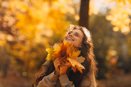 Smiling young woman enjoying the autumn season in the fall park with the yellow leaves at sunsetの写真素材